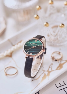 Detail of rose gold watch with green malachite dial and black leather strap on tray