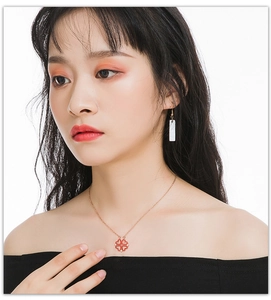 Detail of red clover pendant necklace and white earrings on model for a trendy look