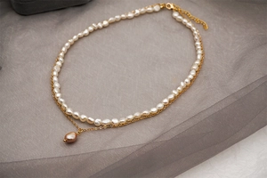 Détail d'un collier doré à plusieurs rangs avec perles baroques et pendentif violet
