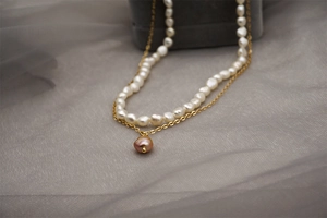 Gros plan sur un collier double rang en perles baroques avec chaîne dorée et pendentif