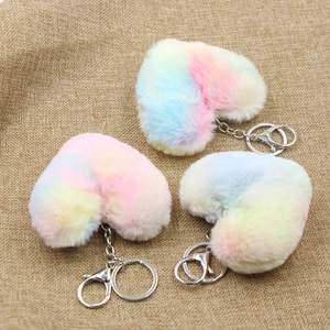 Three colorful rainbow gradient heart plush keychains on rustic linen background