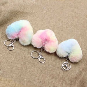 Detailed close-up of three rainbow faux fur heart-shaped plush keychains on burlap background