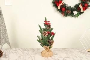 Mini Christmas tree with red berries and pine cones in burlap base on marble table