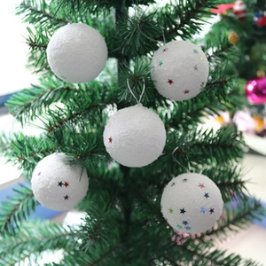 Close-up of white Christmas decorative balls with colorful stars hanging on green tree branches