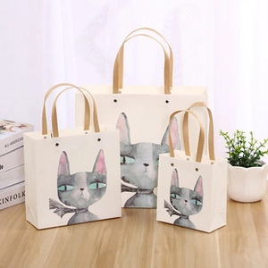 Three assorted sizes of cat-printed gift bags with brown handles on a desk