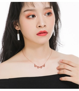 Close-up of elegant gold necklace with five red heart charms worn by female model