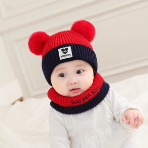 Detail of baby knitted hat and scarf set with red pom-poms and soft wool texture