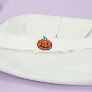 Close-up of Halloween pumpkin enamel pin attached to a white canvas shoulder bag strap