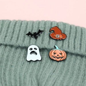 Detail of Halloween ghost and pumpkin enamel pins set on green knitted fabric
