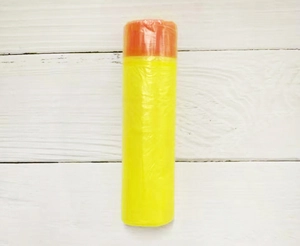 Close-up of yellow drawstring trash bags roll with orange ties on white wood surface