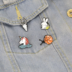 Close-up of animal enamel pins on denim jacket showing unicorn and snail details