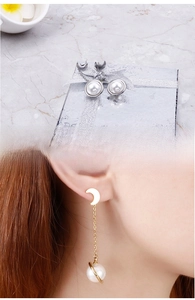 Détail de boucles d'oreilles lune et perle dorées portées et sur boîte cadeau