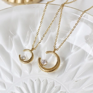 Close-up of crescent moon gold necklaces with round crystals on textured glass tray