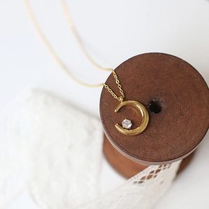 Detail view of 18K gold crescent moon pendant with sparkling round zircon on wooden spool