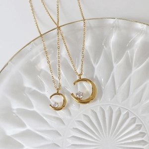 Detailed comparison of two 18K gold crescent moon necklaces with embedded zircons on glass