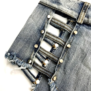 Dettaglio di pantaloncini di denim azzurro con rivetti in metallo e bordi con frange