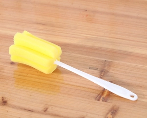 Macro shot of a yellow sponge cleaning brush with a white plastic handle on a wooden surface