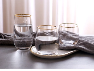 Detail view of gold-rimmed glass cups and matching white tray on a soft grey textile