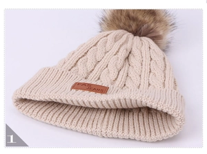 Detail of cable knit pattern and leather patch on beige winter hat with pom-poms