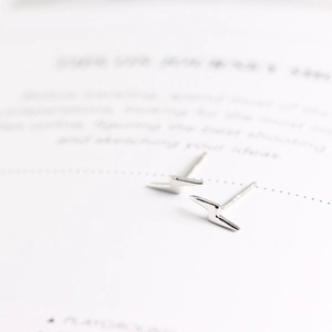 Macro shot of silver lightning bolt stud earrings against a vintage book background