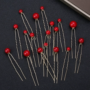 Detail view of red pearl U-shaped hair pins with gold metal finish on black background