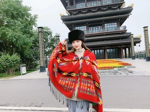 Outdoor shot of a woman wearing a red geometric poncho and black faux fur hat