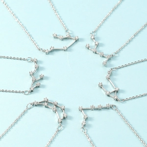 Minimalist silver zodiac necklaces with crystal constellations on light blue background