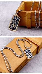 Macro detail of rectangle leopard print pendant with gold cross on a silver box chain