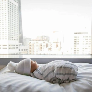 Cozy newborn baby wearing a white knit beanie with pom pom and a grey striped swaddle