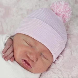 Detail of pink knitted newborn hat with fluffy pom-pom on baby model in soft lighting