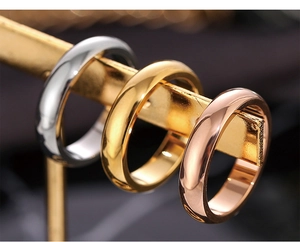 Close-up of three polished stainless steel band rings in silver, gold, and rose gold finishes