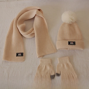 Detail of knitted beanie with pompom, scarf and touchscreen gloves in beige