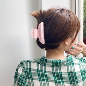 Large marbled pink acetate hair claw clip holding long hair in a bun hairstyle