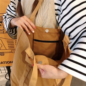 Detail showing the magnetic buckle closure and internal zipper pocket of the brown canvas tote