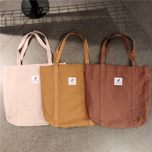 Flat lay of canvas tote bags in cream, mustard, and brown with 'You need this one' labels