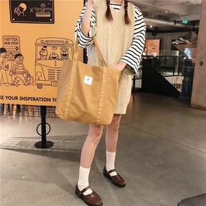 Lifestyle shot of a khaki canvas tote bag worn by a model in a casual indoor setting