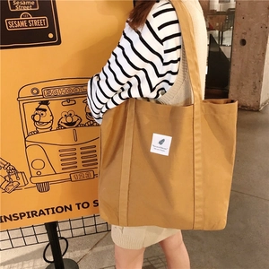 Detail of mustard yellow canvas tote bag with feather print patch worn on shoulder