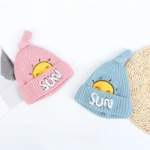 Detailed view of pink and blue thick knit baby beanies featuring sun embroidery and knot top