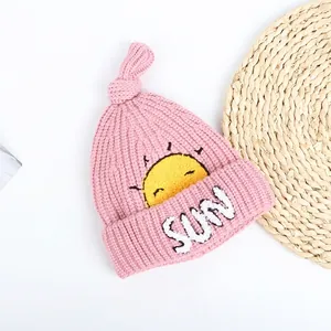 Detail of pink knitted baby hat featuring sun embroidery and knotted top design