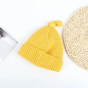 Detailed texture of yellow knitted baby hat with top knot design and ribbed pattern