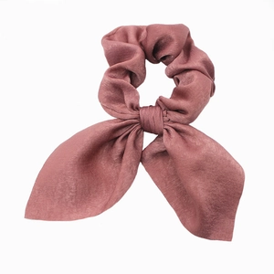 Detail of dusty rose satin hair scrunchie with elegant bow and silk-like texture