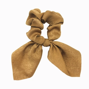 Close-up of brown satin scrunchie with long bow tail showing smooth fabric texture