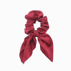 Detailed view of a wine red satin hair scrunchie with a long bow ribbon on white background