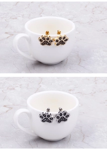 Macro detail of gold and silver paw-shaped earrings with black and white rhinestones