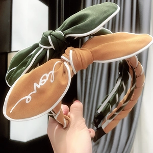 Close-up of woven fabric headbands in green and brown with bow and Love text detail