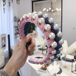 Pink and blue velvet headband with large white pearls held in a stylish indoor setting