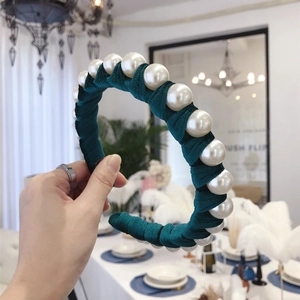 Emerald green velvet headband with large pearls, held in a sophisticated indoor setting