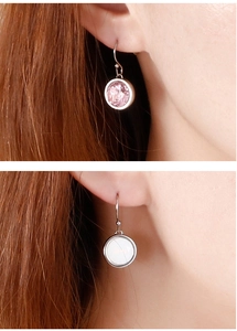 Detail of round earrings featuring pink crystal and white shell on model for visual scale