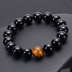Detailed view of polished black onyx beads and a single tiger eye stone on a leather surface