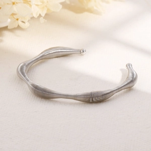 Silver wavy spring-texture stainless steel open bangle on a cream fabric background